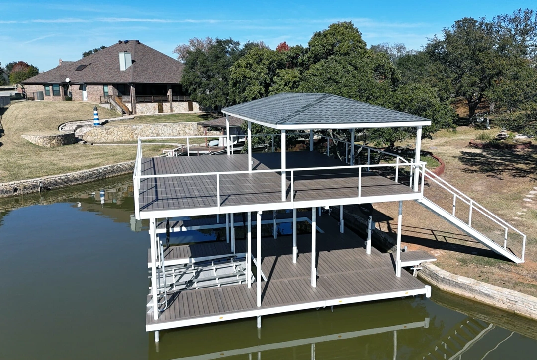 A stunning two-story dock on Lake Granbury featuring a spacious upper deck with a covered pavilion. The dock’s white railings and wooden decking create a modern aesthetic, complementing the serene lakeside setting.